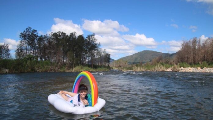 A young woman floats on a flotation device shaped like a cloud and rainbow in Cattle Creek